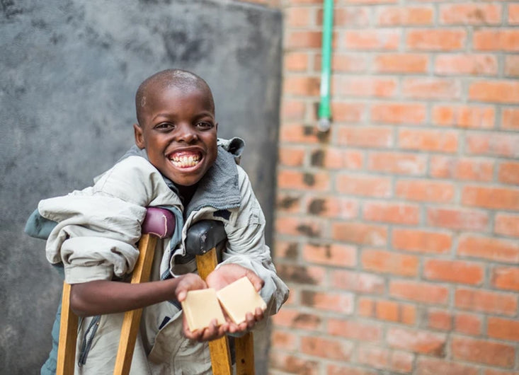 Young African child on crutches holding two bars of goat milk soap from Bend Soap Co.