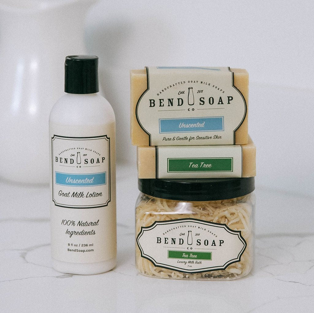 The Best for Acne Bundle from Bend Soap Co.—featuring unscented goat milk lotion, two goat milk soap bars, tea tree essential oil soap, and an unscented luxury milk bath—is arranged on a white surface.