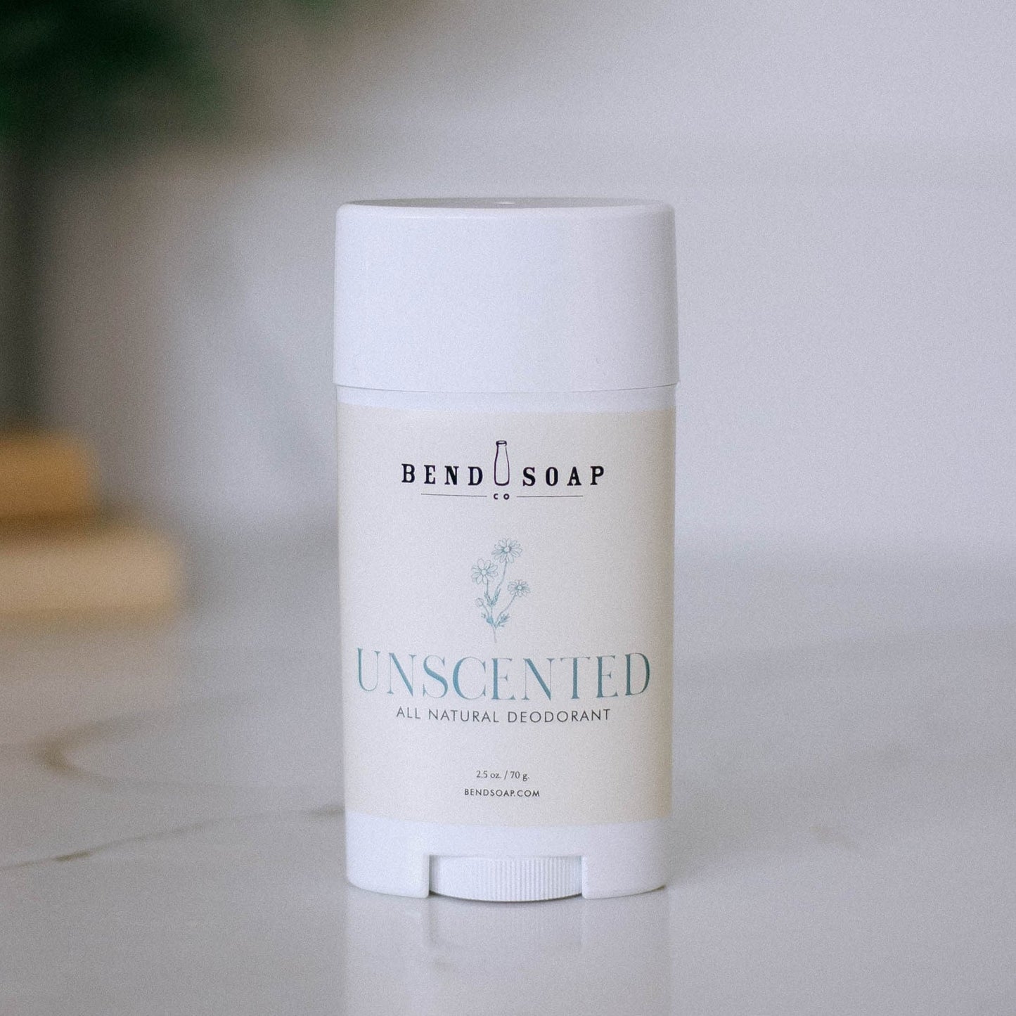 An upright stick of Unscented Magnesium Deodorant (Baking Soda Free) sits on a light surface with a blurred background. The white label features minimalist text, emphasizing its gentle, baking soda–free magnesium formula.