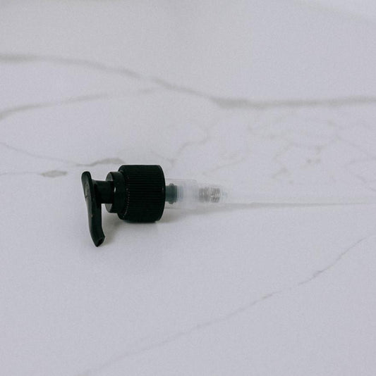 A black plastic Lotion Pump, sized for 8 oz. bottles, is shown detached and lying sideways on a white marbled surface. No bottle, like a goat milk lotion container, is included or pictured.