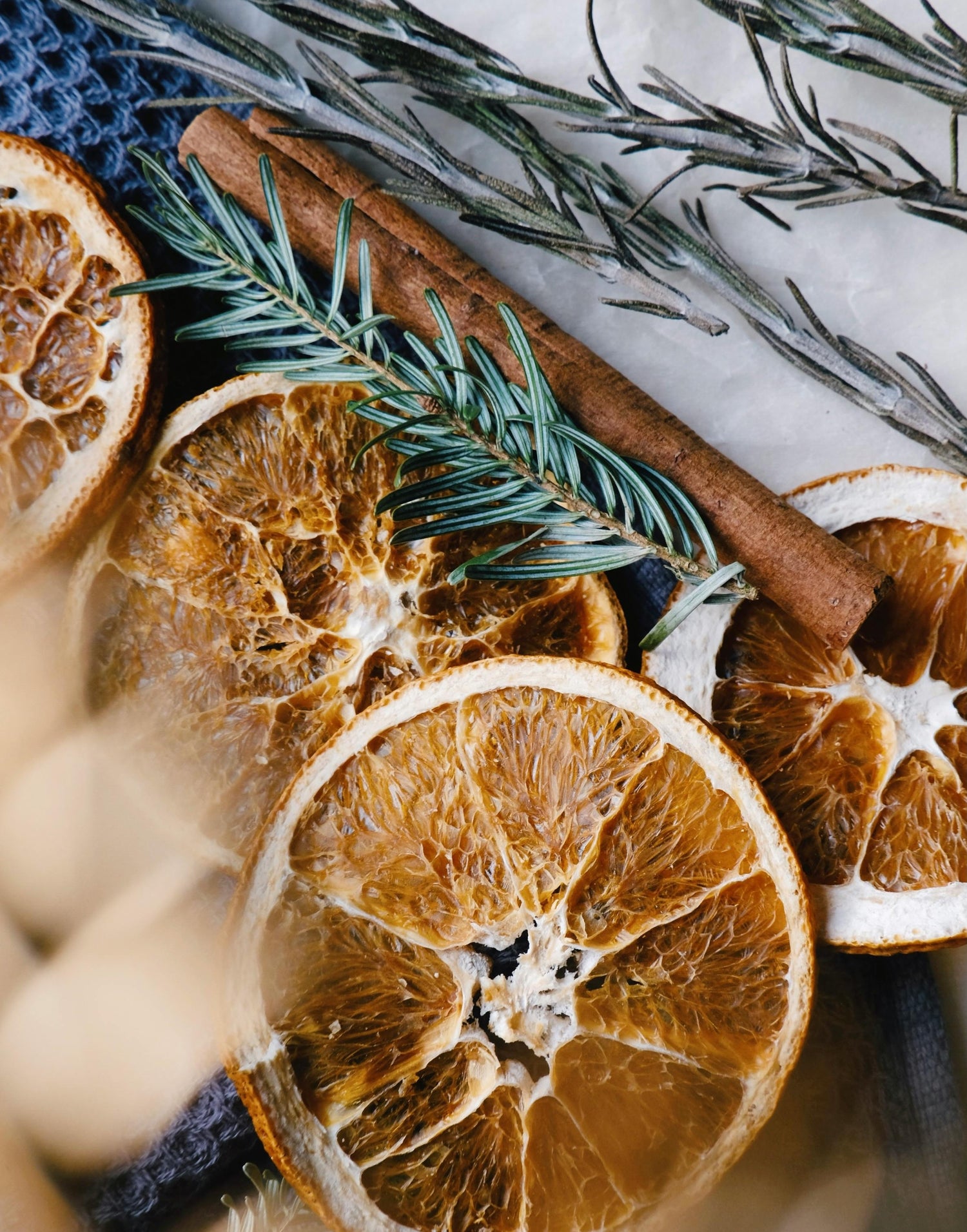 Dried orange slices, a cinnamon stick, and sprigs of rosemary arranged together on a textured surface, creating a rustic, aromatic display.