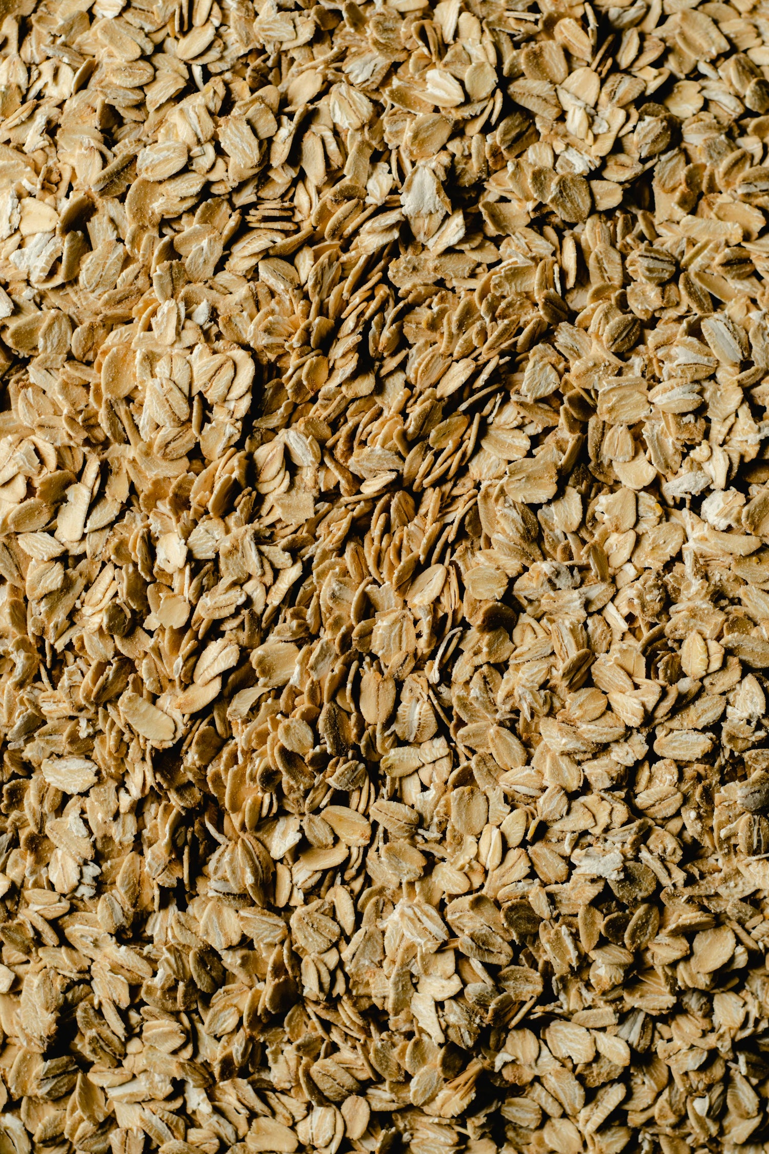 A close-up view of a large pile of dry rolled oats, showing their rough, flat texture and light brown color.