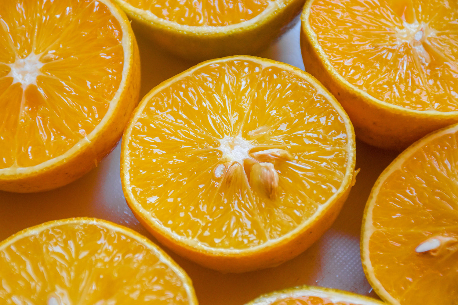 Close-up of several fresh orange halves with visible seeds and juicy, vibrant orange flesh arranged closely together.
