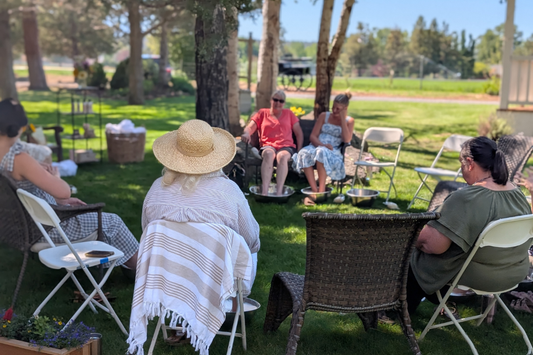 Group of women enjoying a spa night at home outdoors with foot soak bowls, creating a relaxed DIY spa day with friends in a cozy backyard setting