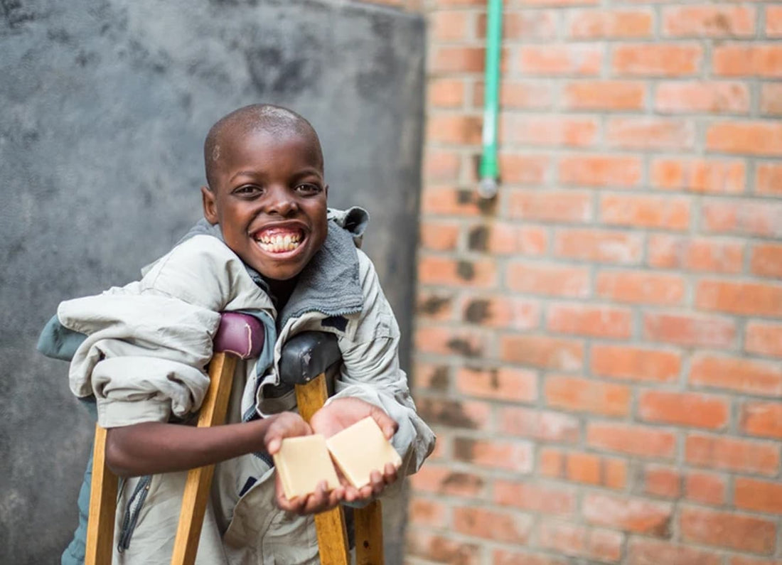 Young African child on crutches holding two bars of goat milk soap from Bend Soap Co. 