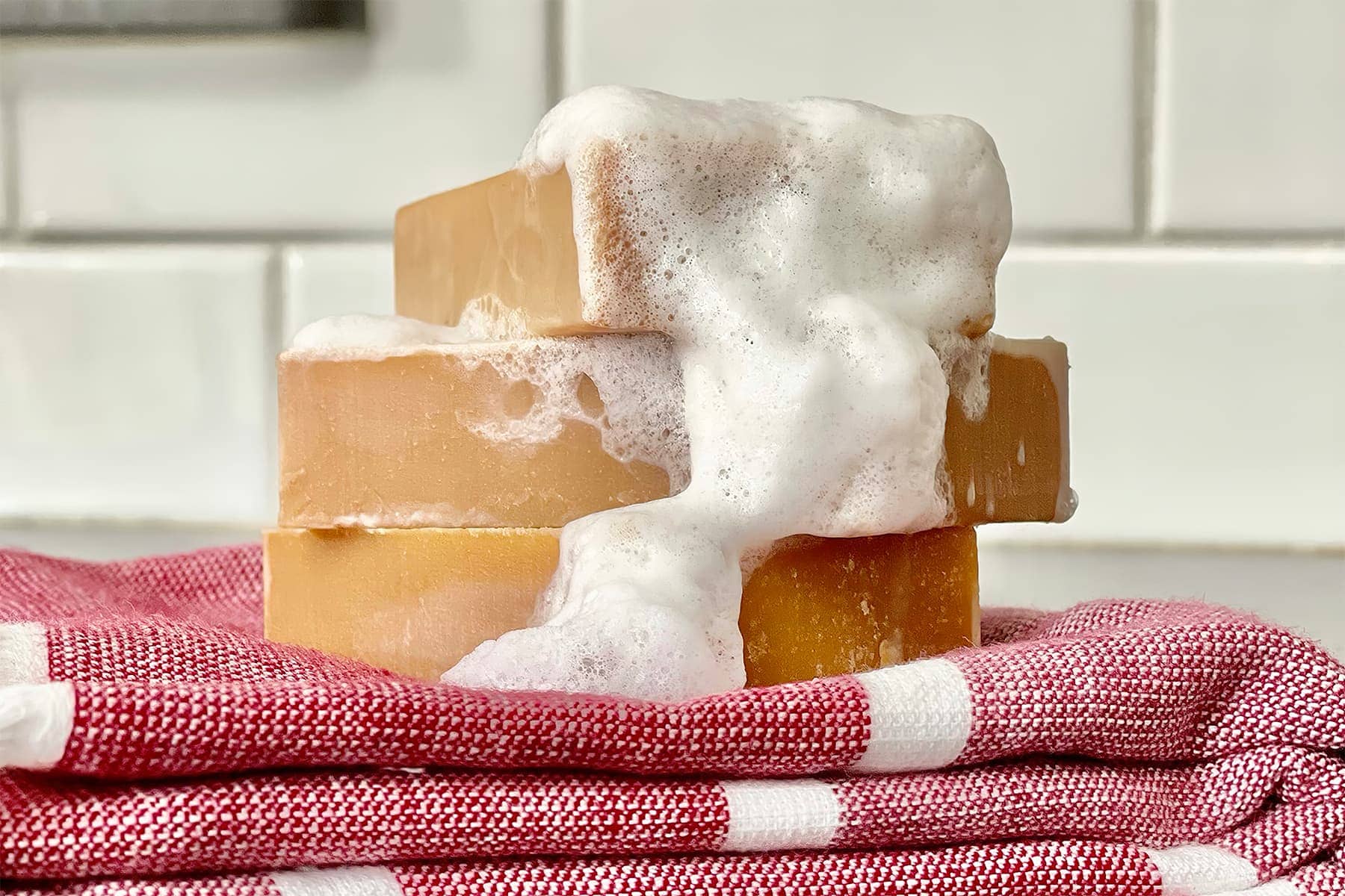 a stack of three bars of chai tea goat milk soap covered in soap suds