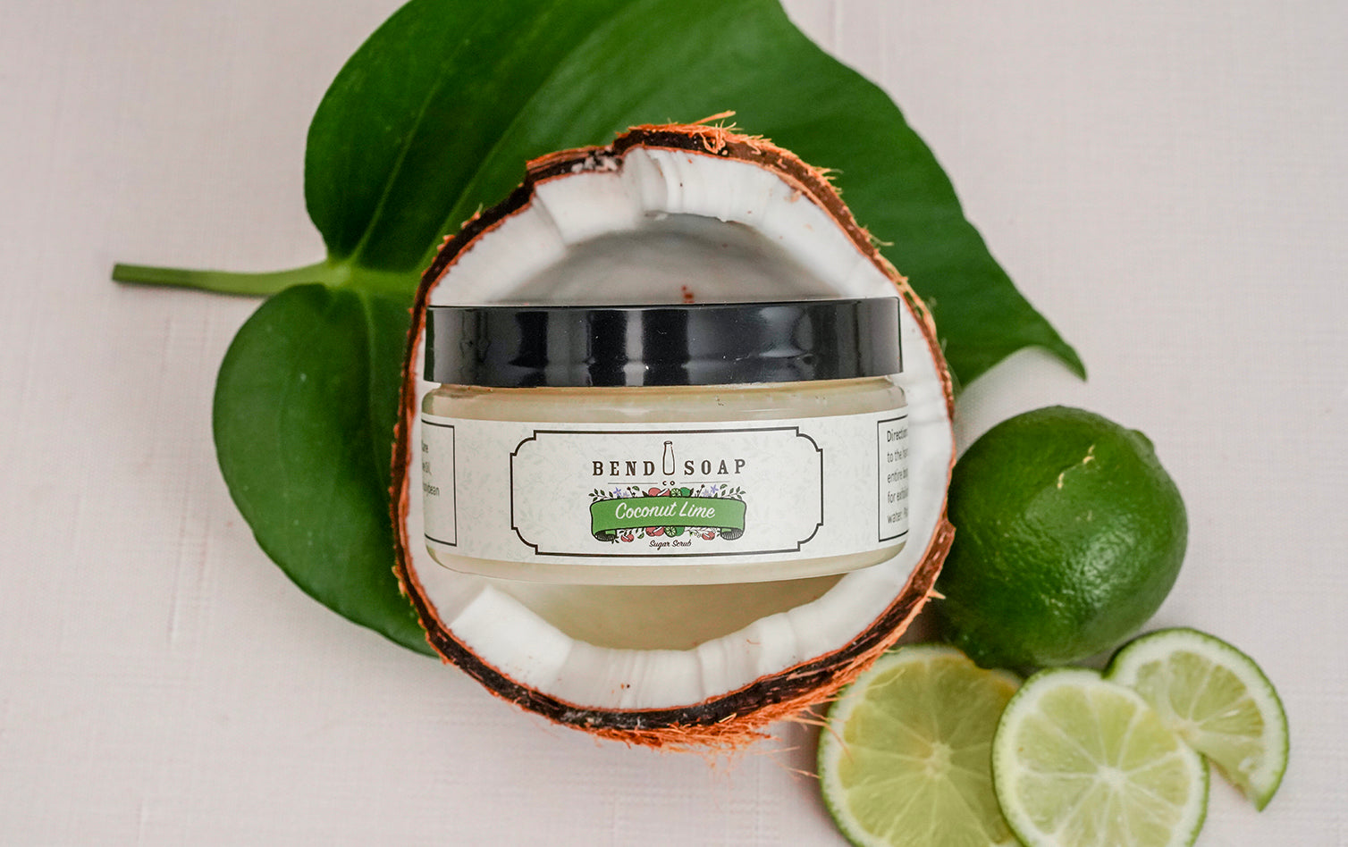 Coconut Lime Sugar Scrub on in a Halved Coconut on Top of a Tropical Leaf
