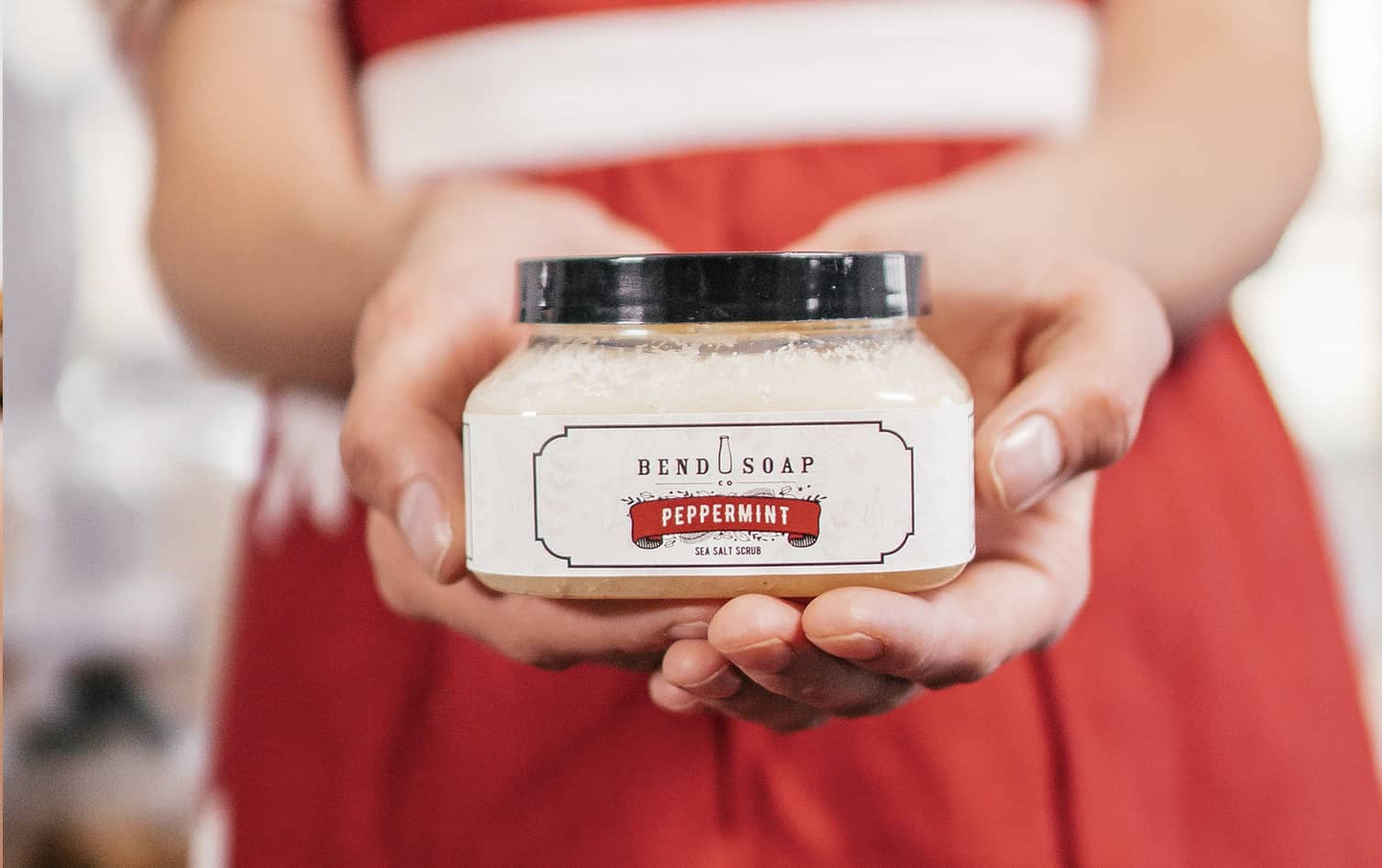 A woman dressed in red holding a tub of limited edition peppermint sea salt scrub