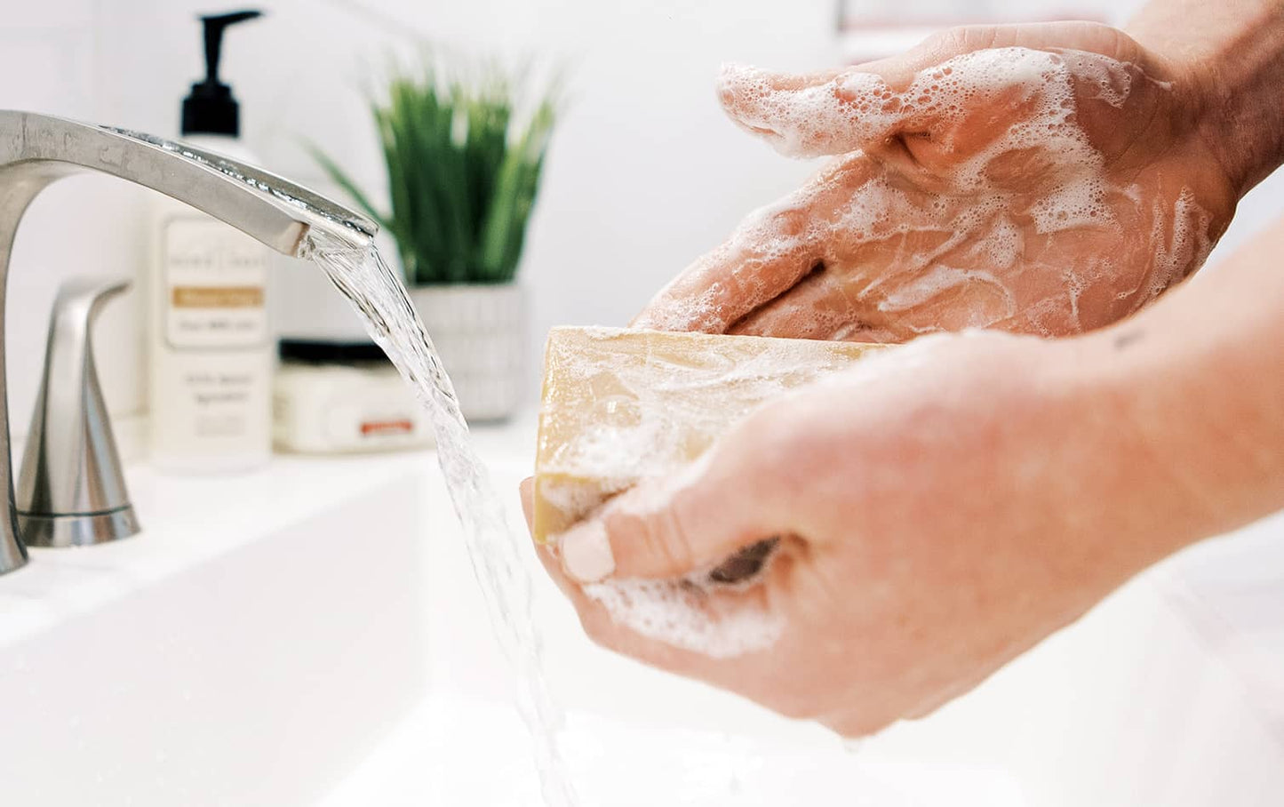 A woman washing her hands in a white sink with peppermint goat milk soap